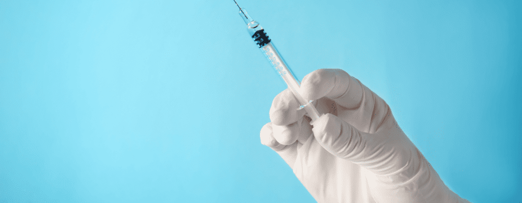 gloved hand holding a syringe